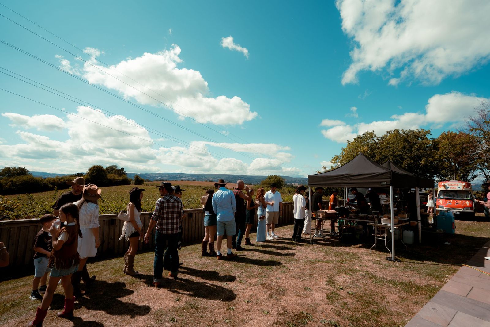 Guests in cowboy hats queuing at the food gazebo at a countryside garden party